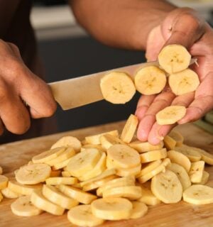 Photo shows a young African man's hands as he chops plantain in the kitchen