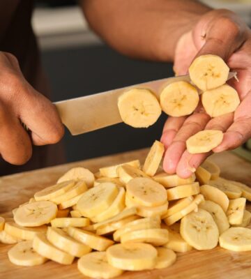 Photo shows a young African man's hands as he chops plantain in the kitchen