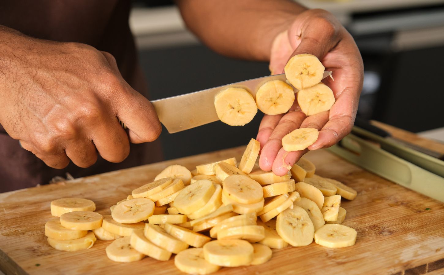 Photo shows a young African man's hands as he chops plantain in the kitchen