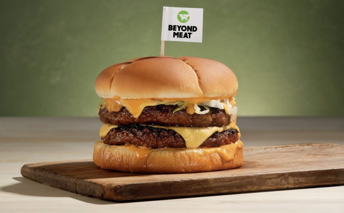 Photo shows a plant-based burger on a wooden board with a small Beyond Meat flag on a toothpick