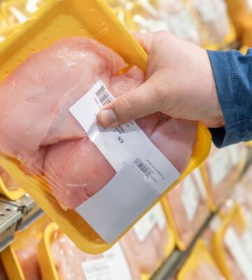 A person picking up a chicken breast from a supermarket shelf