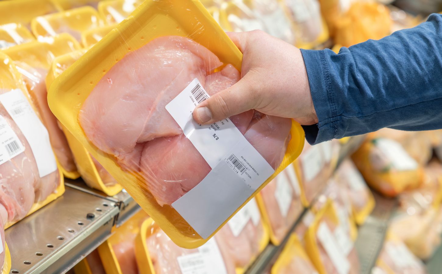 A person picking up a chicken breast from a supermarket shelf