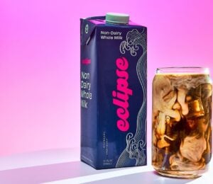 Photo shows a carton of the new plant-based whole milk from Eclipse Foods next to an iced coffee, set against a pink background