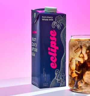 Photo shows a carton of the new plant-based whole milk from Eclipse Foods next to an iced coffee, set against a pink background