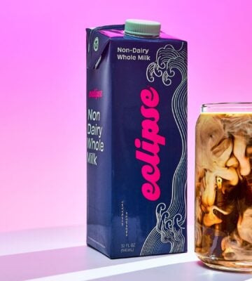 Photo shows a carton of the new plant-based whole milk from Eclipse Foods next to an iced coffee, set against a pink background