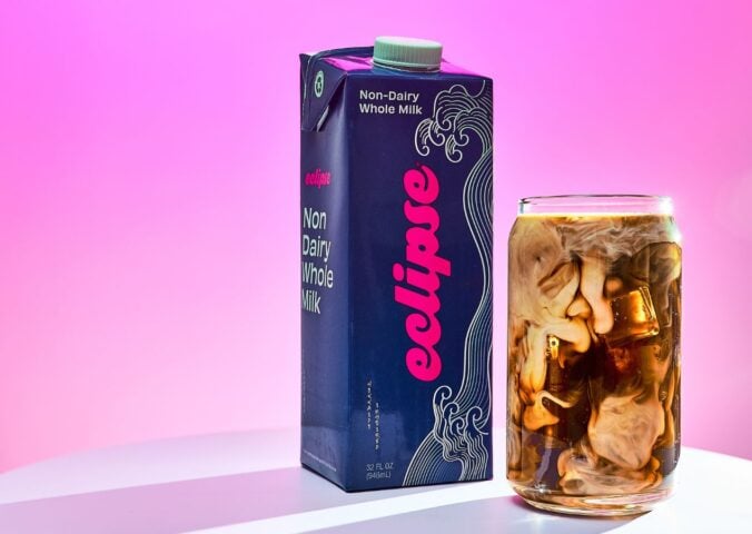 Photo shows a carton of the new plant-based whole milk from Eclipse Foods next to an iced coffee, set against a pink background