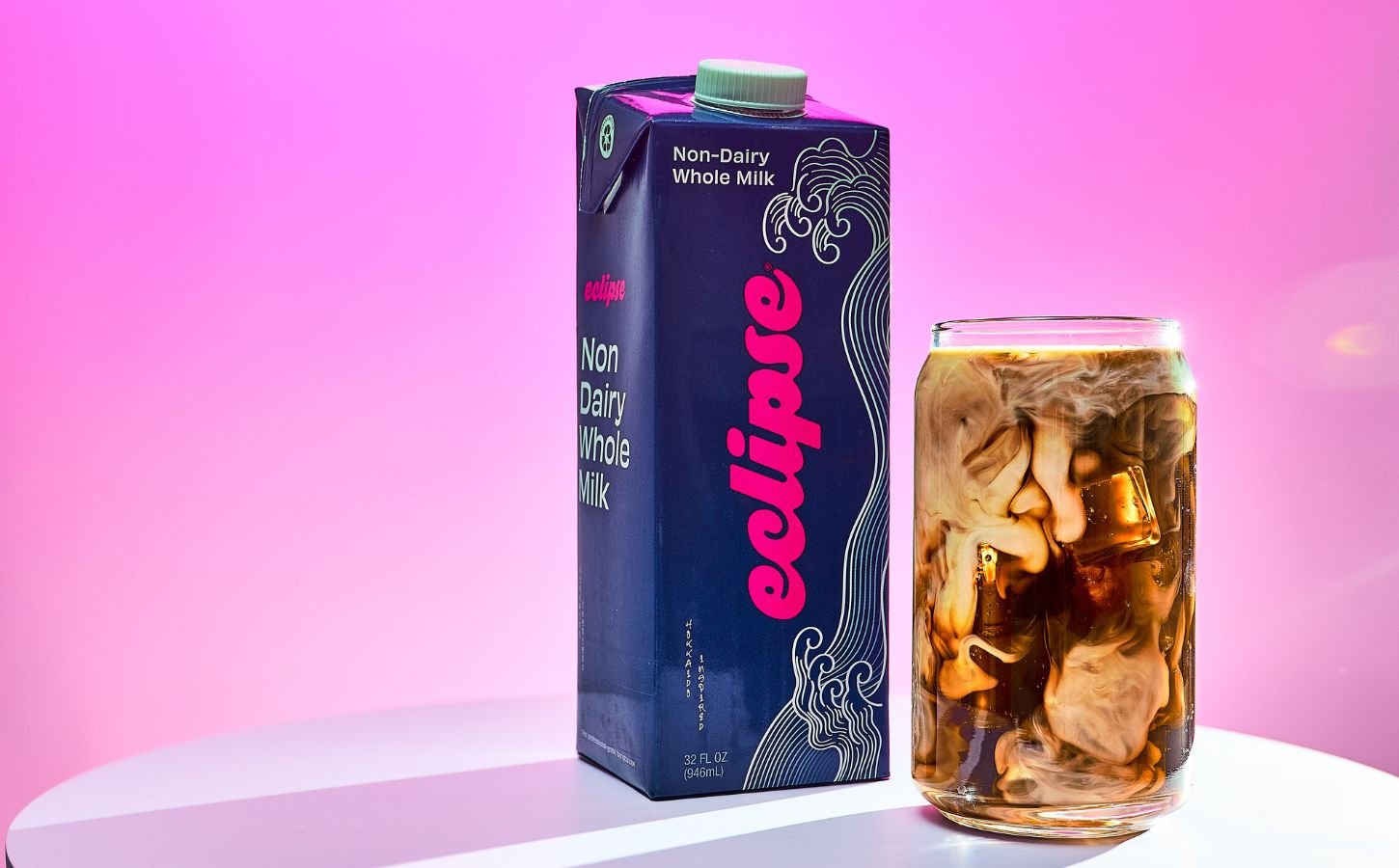 Photo shows a carton of the new plant-based whole milk from Eclipse Foods next to an iced coffee, set against a pink background