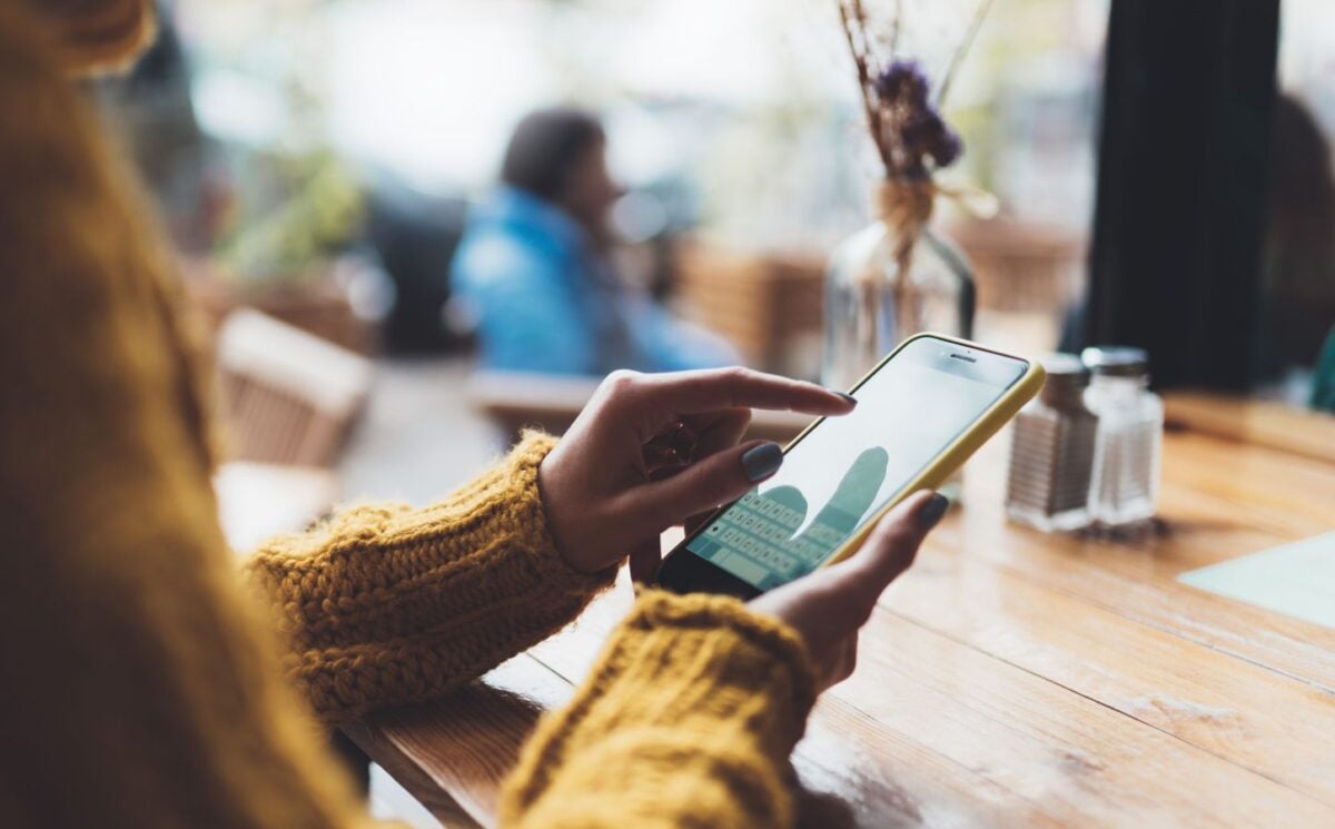 Photo shows someone typing on her phone while sat at a wooden table