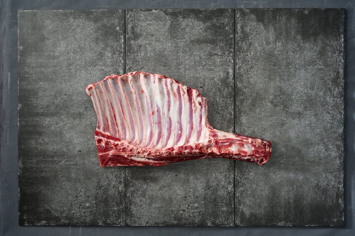 Photo shows a rack of raw lamb meat against a dark stone surface