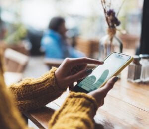 Photo shows someone typing on her phone while sat at a wooden table