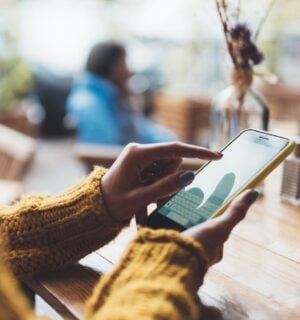 Photo shows someone typing on her phone while sat at a wooden table