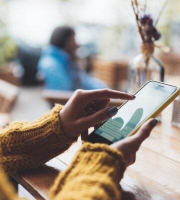 Photo shows someone typing on her phone while sat at a wooden table