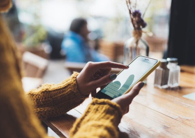 Photo shows someone typing on her phone while sat at a wooden table