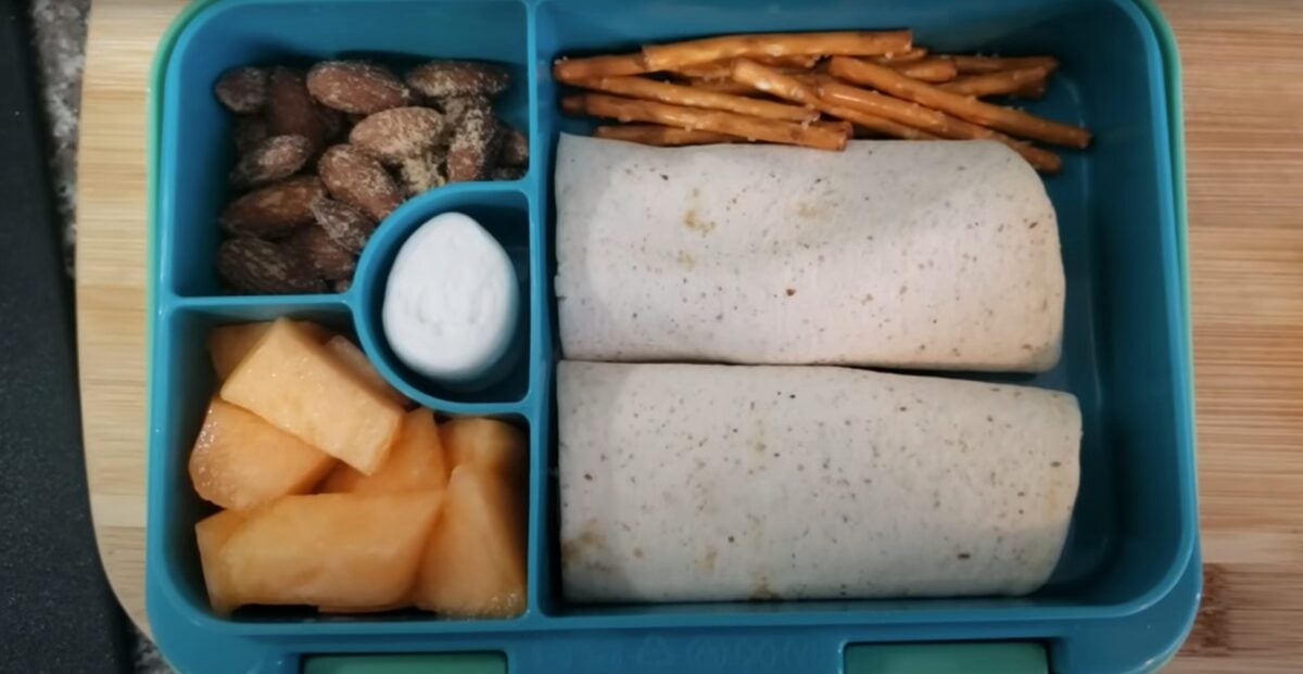 A vegan kids packed lunch featuring an apple and peanut butter wrap