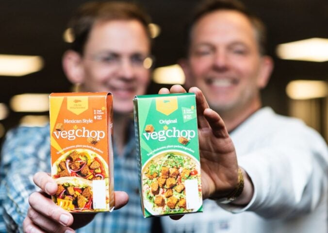 Photo shows Oh So Wholesome founders Jason Gibb and Simon Day holding up packets of their flagship “Veg’chop" product