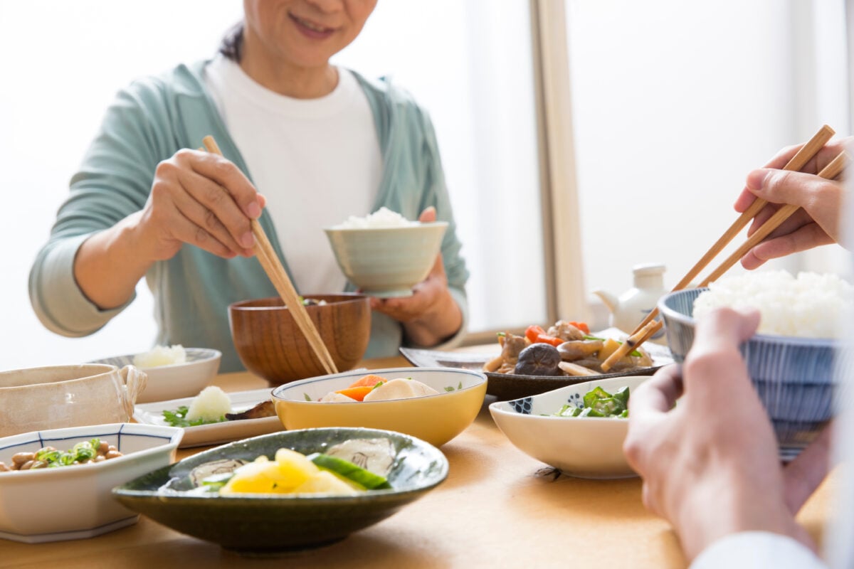 Photo shows a group of people sharing a meal and eating with chopsticks