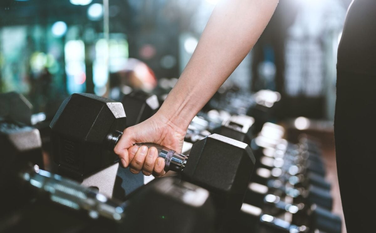 Photo shows a woman's hand as she moves to pick up a dumbbell in a gym