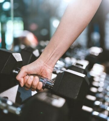 Photo shows a woman's hand as she moves to pick up a dumbbell in a gym
