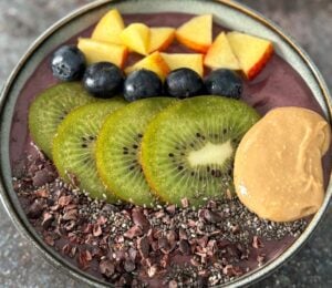 A vegan acai smoothie bowl topped with nectarine, blueberries, and kiwi, a high protein vegan breakfast