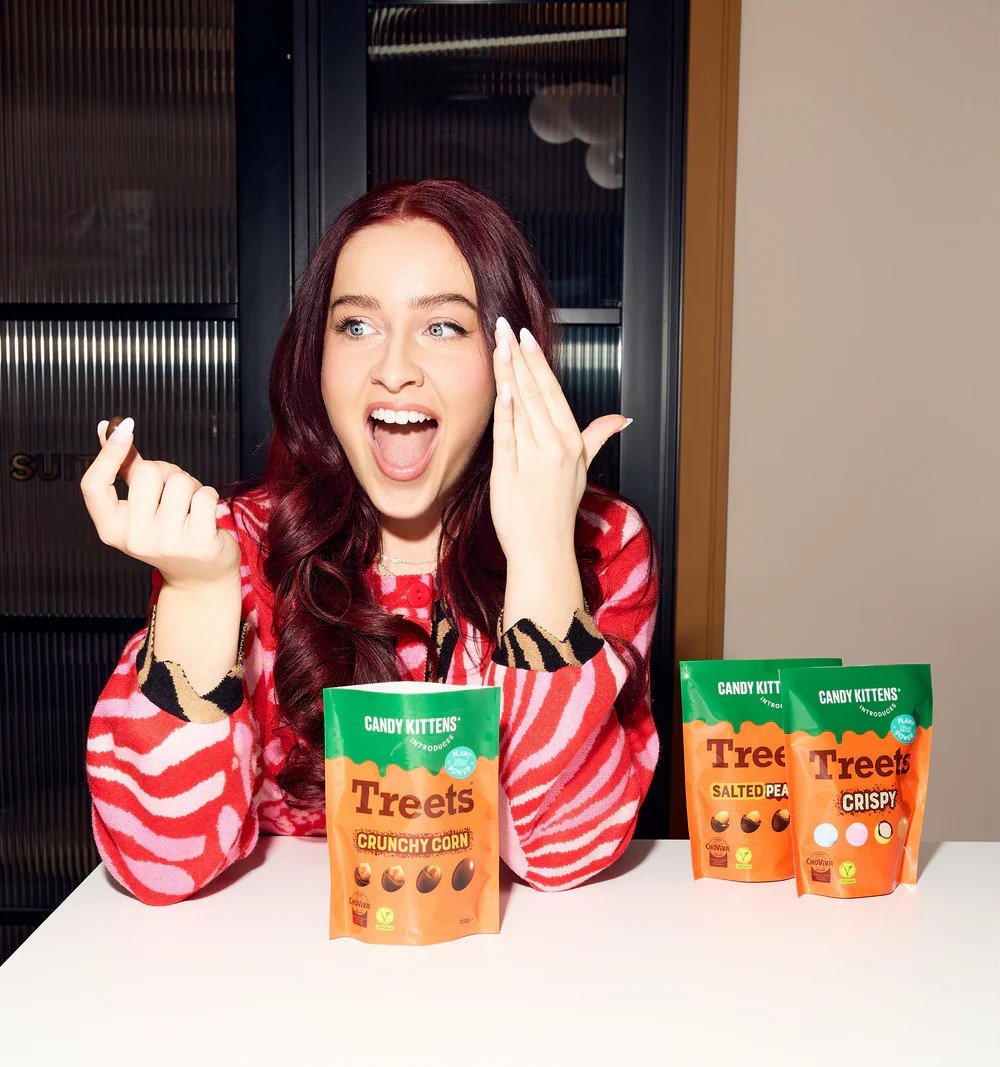 Photo shows a young woman sat at a table eating the new Candy Kittens x Treets vegan chocolates
