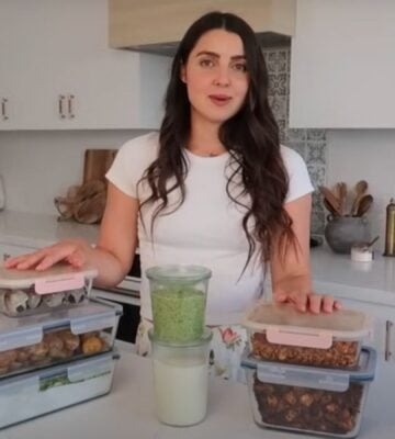 Stephanie Manzinali of That Vegan Babe stands in her kitchen with prepped vegan sauces, proteins, and snacks, ready to create high-protein meals in under two hours using her flexible mix-and-match method.