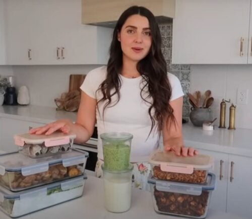 Stephanie Manzinali of That Vegan Babe stands in her kitchen with prepped vegan sauces, proteins, and snacks, ready to create high-protein meals in under two hours using her flexible mix-and-match method.