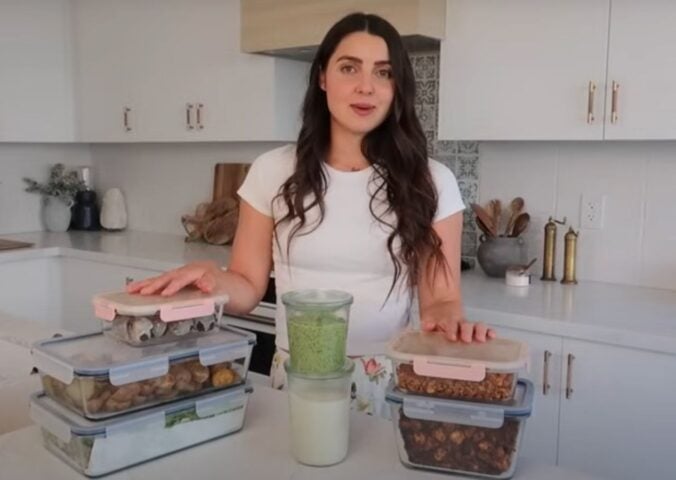 Stephanie Manzinali of That Vegan Babe stands in her kitchen with prepped vegan sauces, proteins, and snacks, ready to create high-protein meals in under two hours using her flexible mix-and-match method.