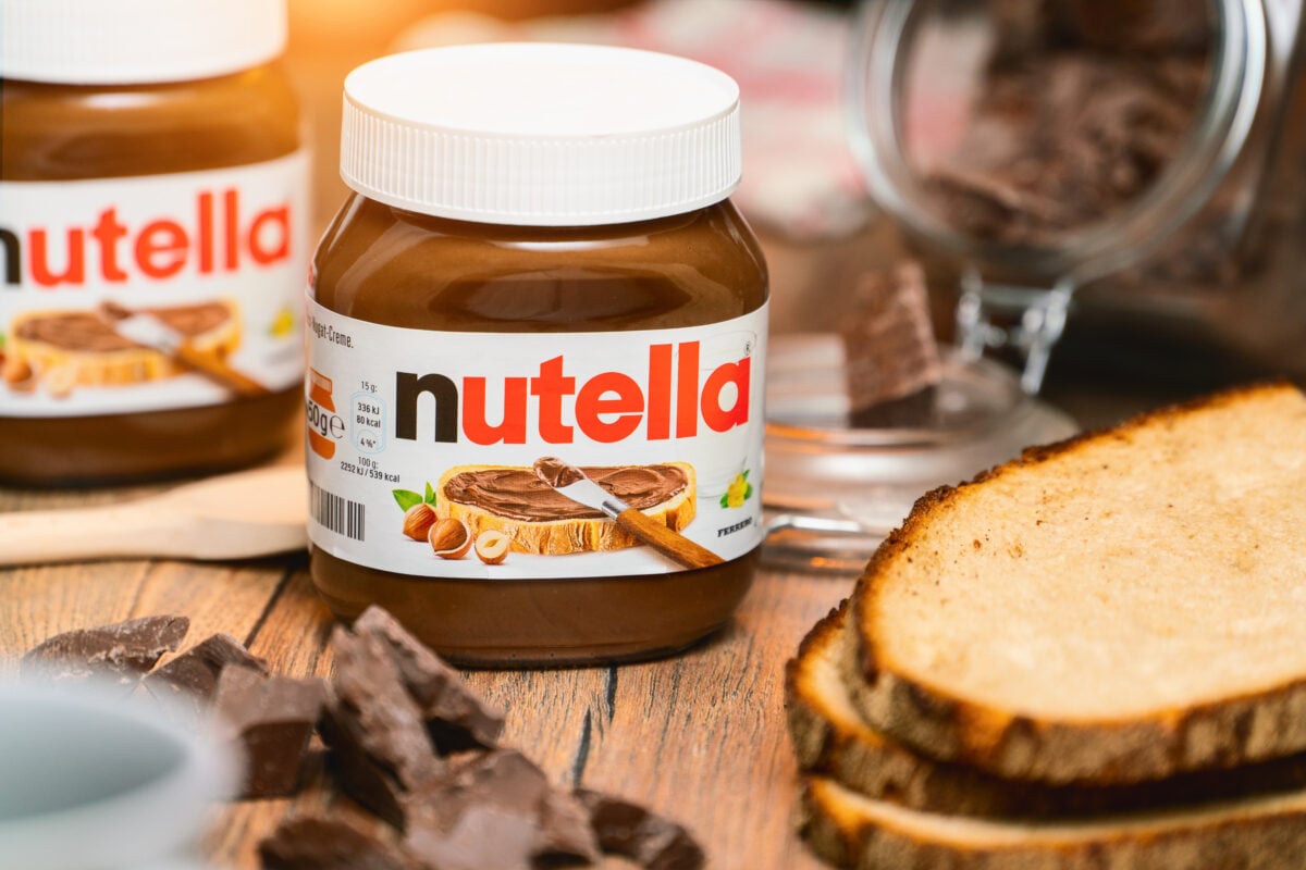 Photo shows a tub of Nutella amongst slices of bread and pieces of chocolate