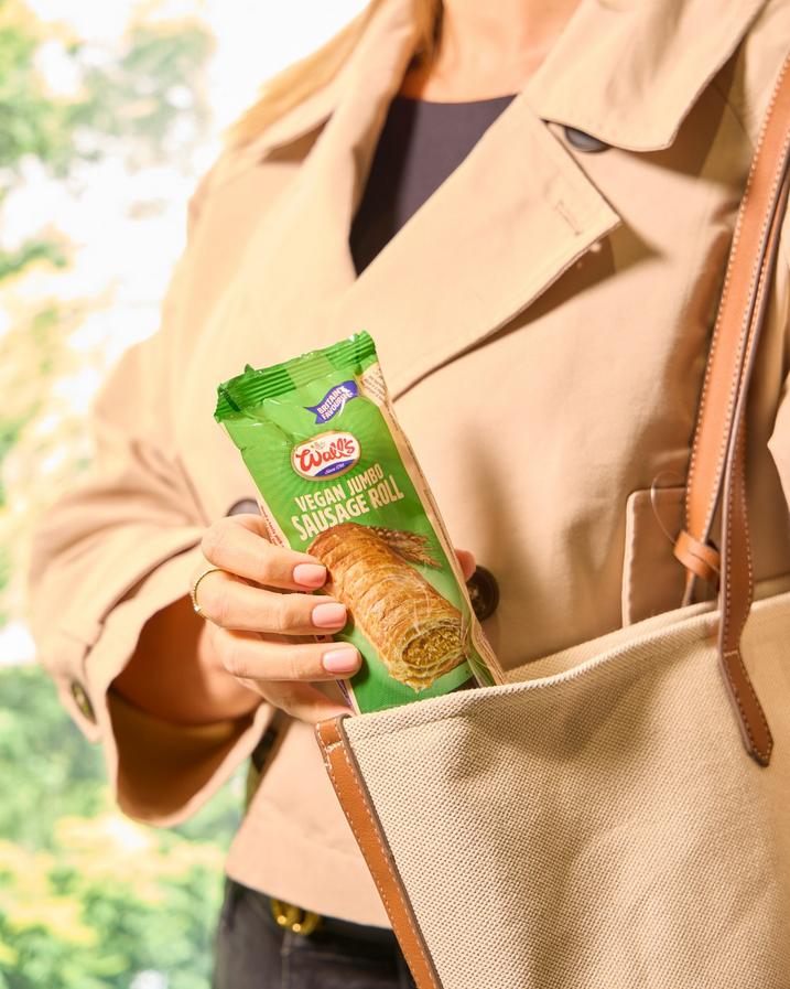 Photo shows someone in a long pink overcoat taking a vegan Wall's sausage roll out of the pocket