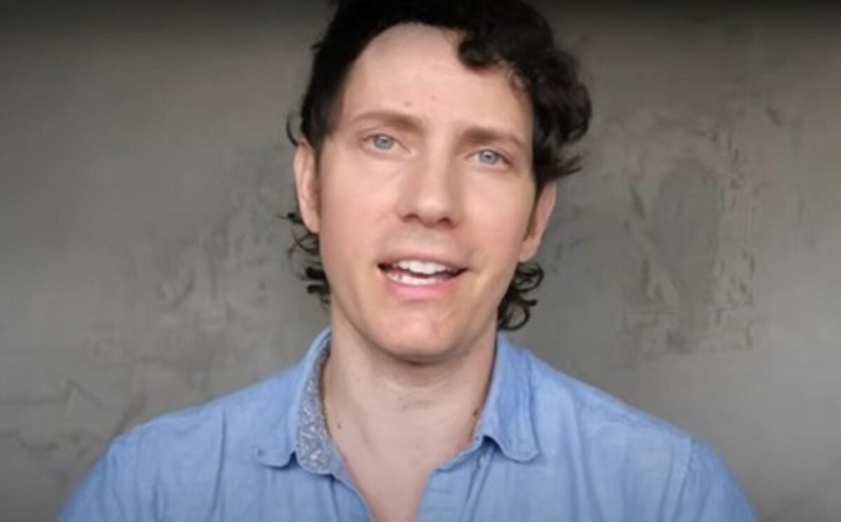 Wearing a light blue shirt over a grey background, Mic the Vegan speaks about plant-based protein.