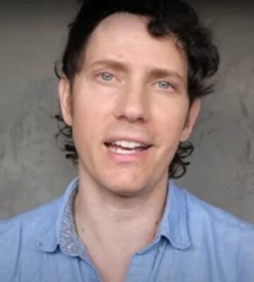 Wearing a light blue shirt over a grey background, Mic the Vegan speaks about plant-based protein.