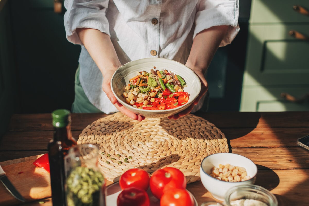 Photo shows a woman holding a bowl of plant-based food