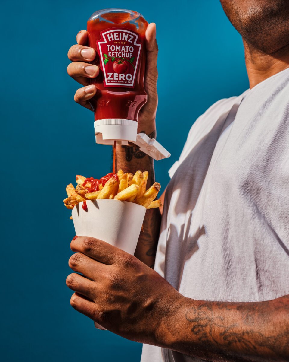 A person pouring Heinz Ketchup on chips