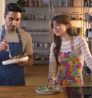 Dr. Rupy Aujla and Sophie Waplington stand by a counter cooking high-protein vegan work lunches