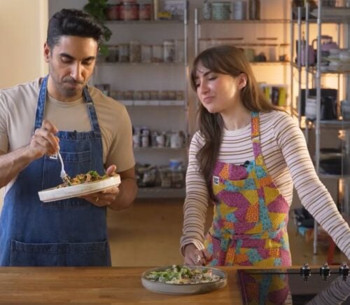 Dr. Rupy Aujla and Sophie Waplington stand by a counter cooking high-protein vegan work lunches