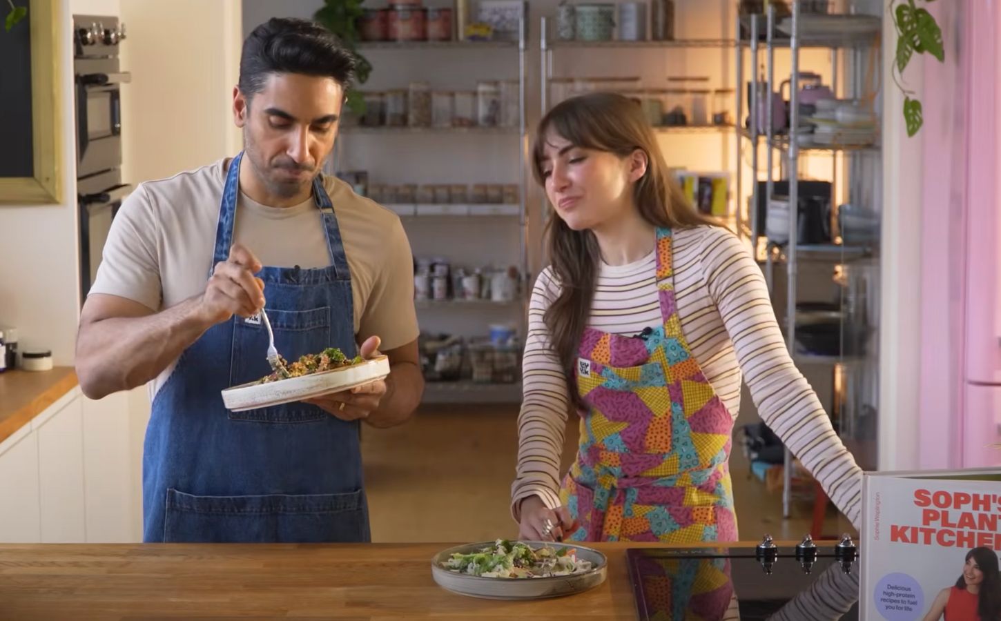Dr. Rupy Aujla and Sophie Waplington stand by a counter cooking high-protein vegan work lunches