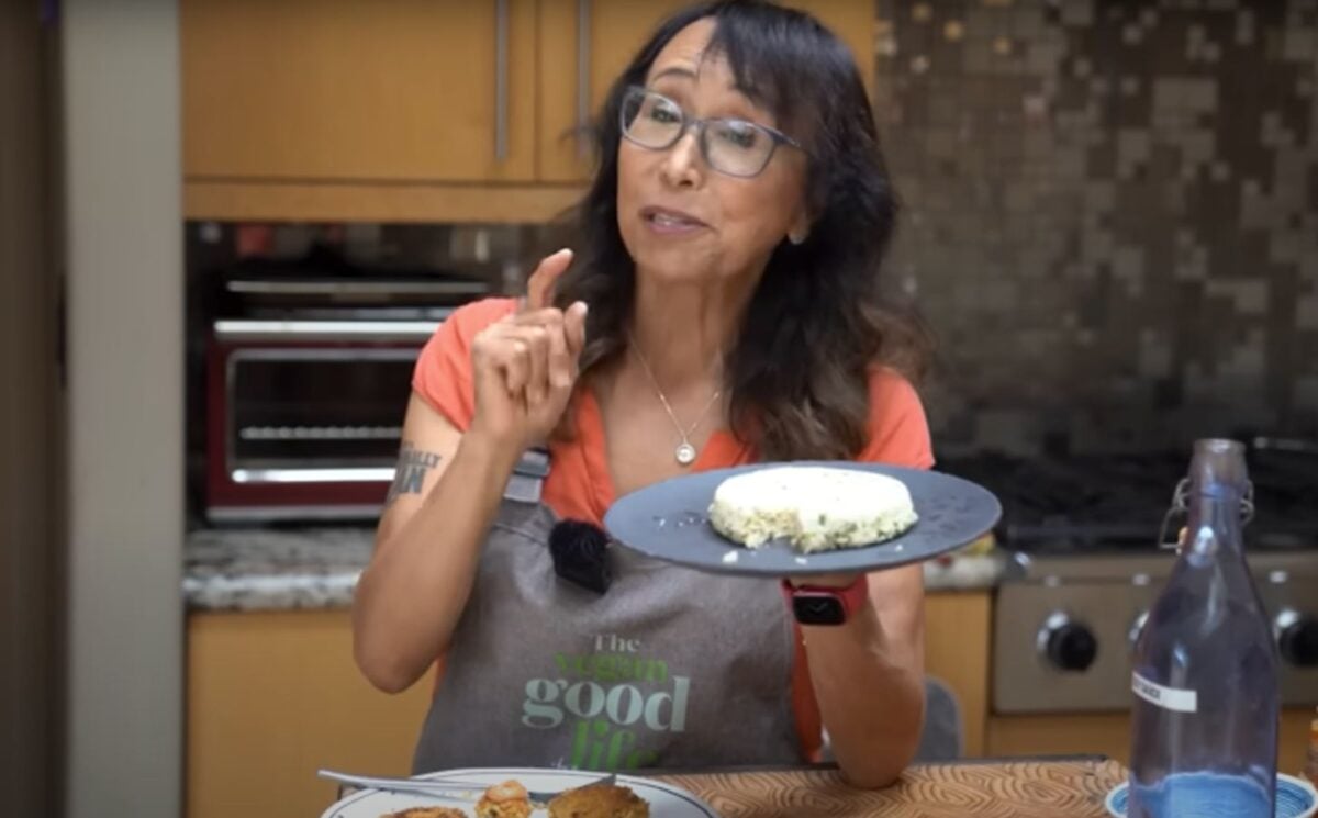Miyoko Schinner standing in a kitchen holding up a plate of homemade tofu with scallions