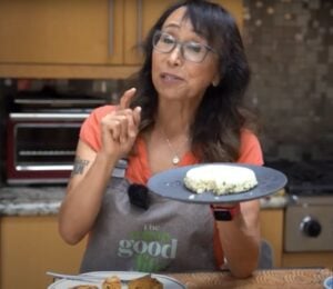 Miyoko Schinner standing in a kitchen holding up a plate of homemade tofu with scallions