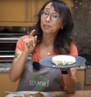 Miyoko Schinner standing in a kitchen holding up a plate of homemade tofu with scallions