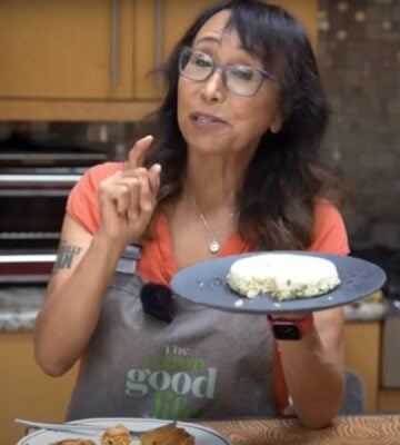 Miyoko Schinner standing in a kitchen holding up a plate of homemade tofu with scallions