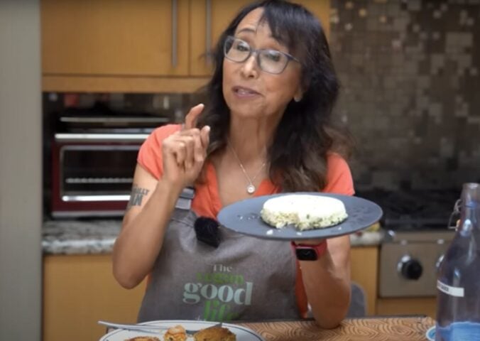Miyoko Schinner standing in a kitchen holding up a plate of homemade tofu with scallions