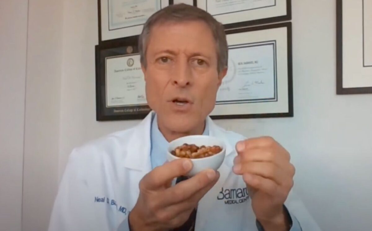 Dr. Neal Barnard holds a small bowl of cooked soybeans while explaining menopause diet tips, with framed certificates visible on the wall behind him