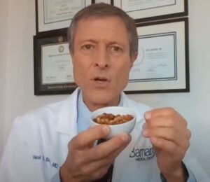 Dr. Neal Barnard holds a small bowl of cooked soybeans while explaining menopause diet tips, with framed certificates visible on the wall behind him