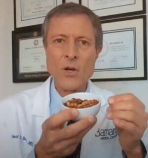 Dr. Neal Barnard holds a small bowl of cooked soybeans while explaining menopause diet tips, with framed certificates visible on the wall behind him