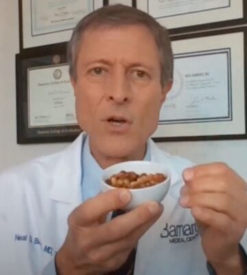 Dr. Neal Barnard holds a small bowl of cooked soybeans while explaining menopause diet tips, with framed certificates visible on the wall behind him