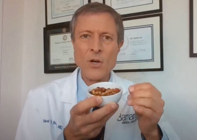 Dr. Neal Barnard holds a small bowl of cooked soybeans while explaining menopause diet tips, with framed certificates visible on the wall behind him