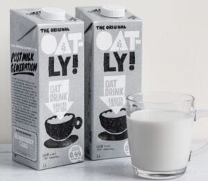 Photo shows two cartons of Oatly Barista next to a glass mug of oat milk
