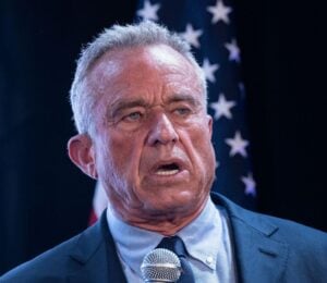 Photo shows RFK Jr speaking into a microphone in front of a US flag