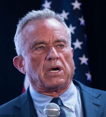 Photo shows RFK Jr speaking into a microphone in front of a US flag