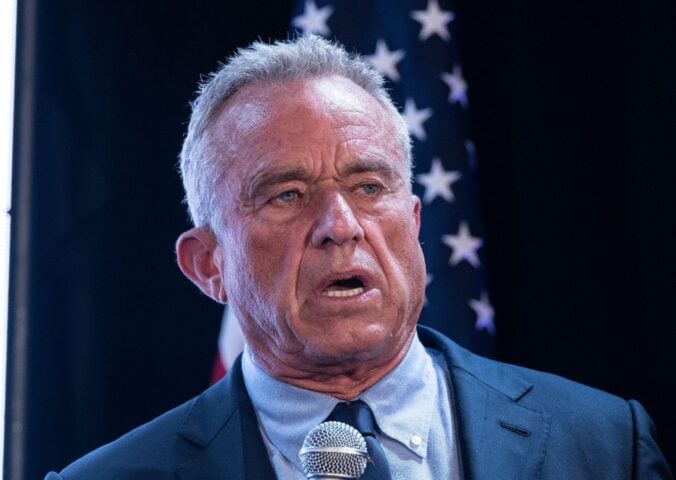 Photo shows RFK Jr speaking into a microphone in front of a US flag